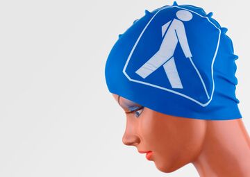 Ansicht auf die blaue Badekappe auf einem Puppenkopf. Ein Stockmännchen ist auf der Kappe abgebildet.