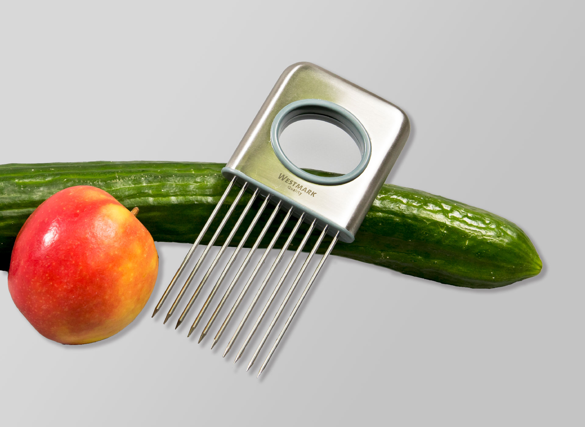 Ansicht auf die Schneidehilfe, gelehnt an einer Gurke und einem Apfel.