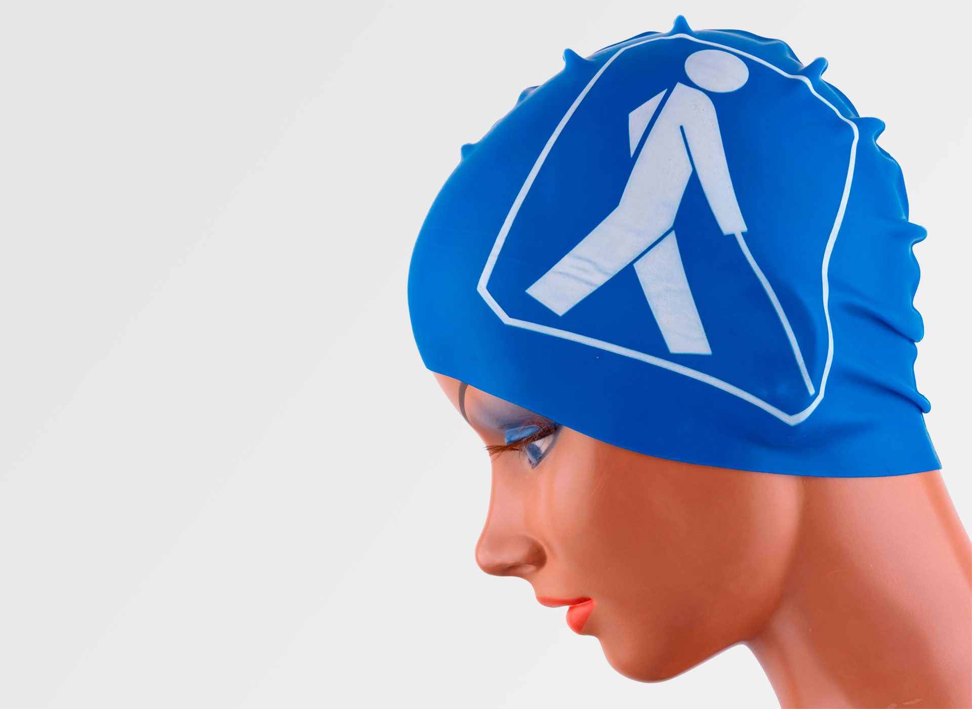 Ansicht auf die blaue Badekappe auf einem Puppenkopf. Ein Stockmännchen ist auf der Kappe abgebildet.